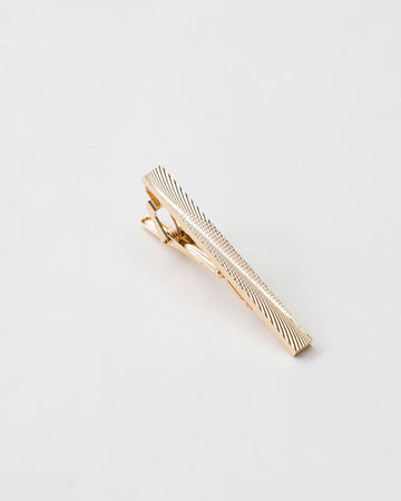 Textured gold-tone tie clip shown with a patterned tie