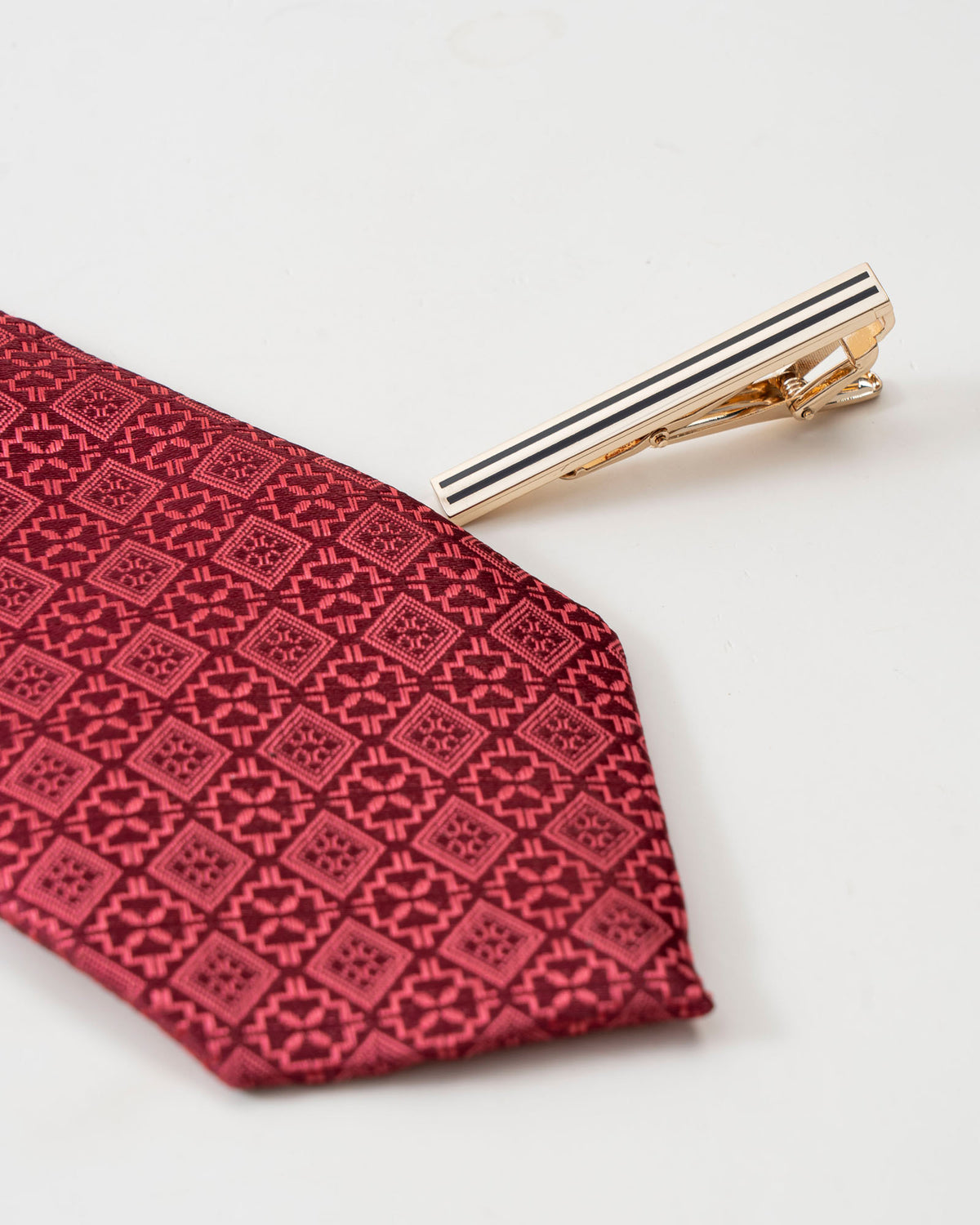 Gold-tone tie clip with black stripes on a patterned red tie