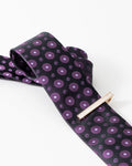 Gold-tone tie clip styled with a black and purple patterned tie