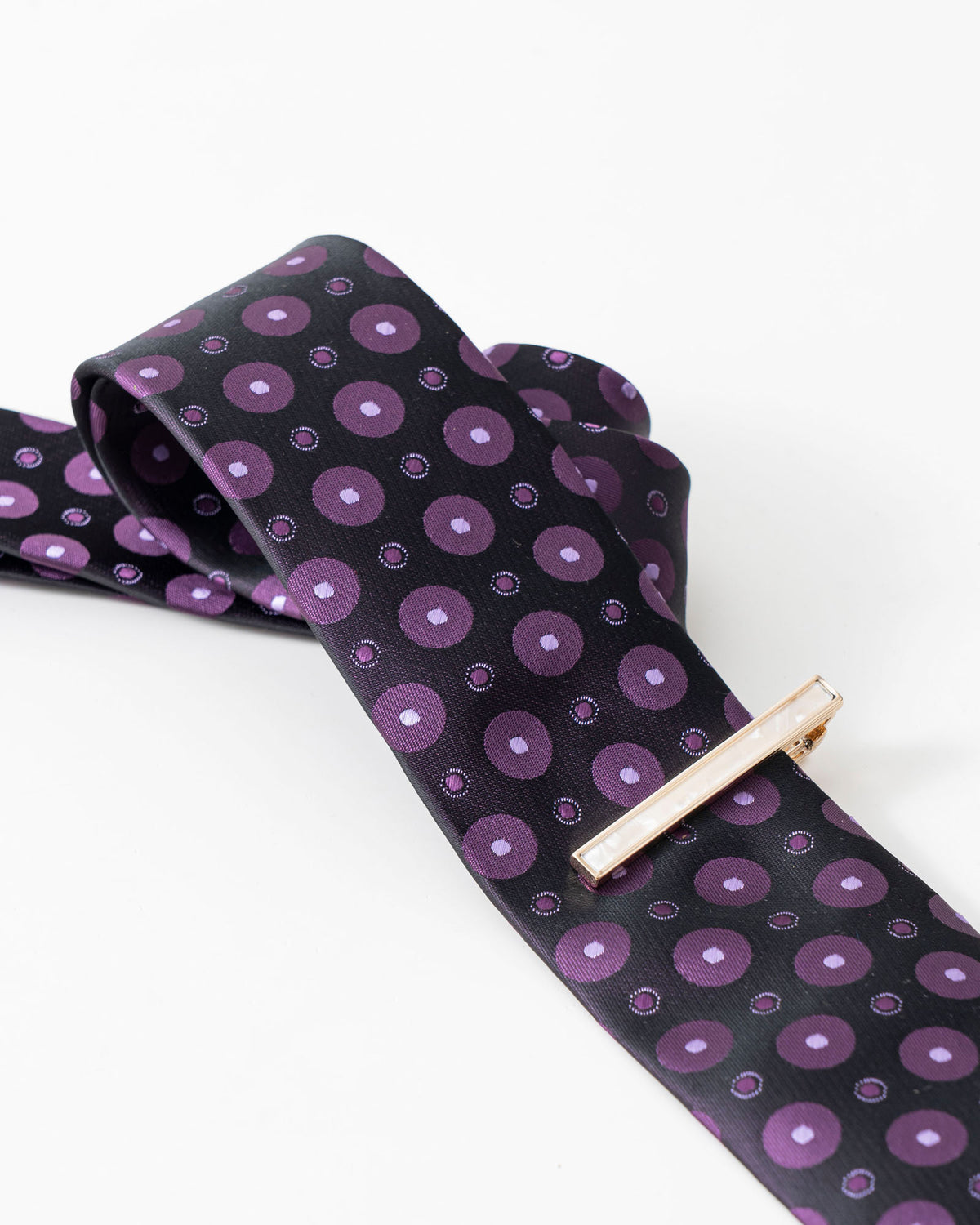Gold-tone tie clip styled with a black and purple patterned tie