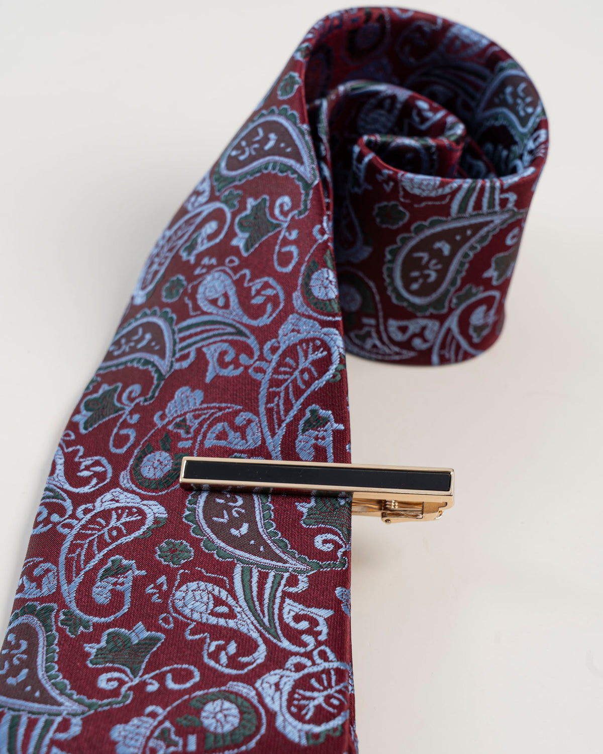 Gold-tone tie clip with black detail paired with a burgundy paisley tie