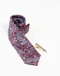 Gold-tone tie clip with black line detailing beside a paisley tie
