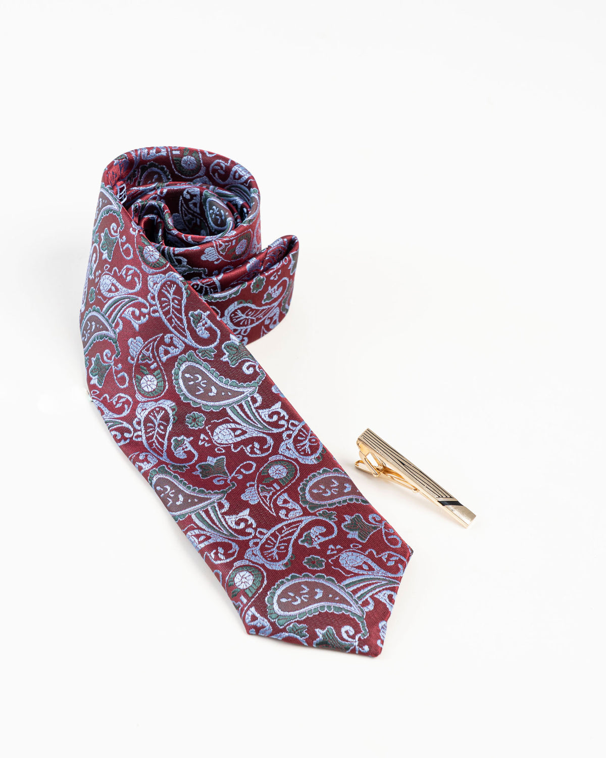 Gold-tone tie clip with black line detailing beside a paisley tie